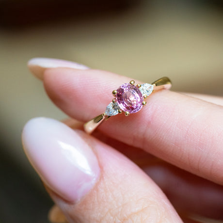 Pink sapphire and diamond three-stone engagement ring with oval pink sapphire centre.