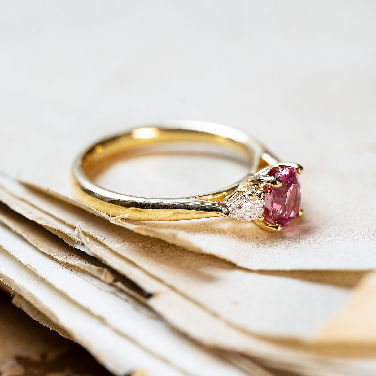 Pink sapphire and diamond three-stone engagement ring with pear-shaped side diamonds and polished gold band.