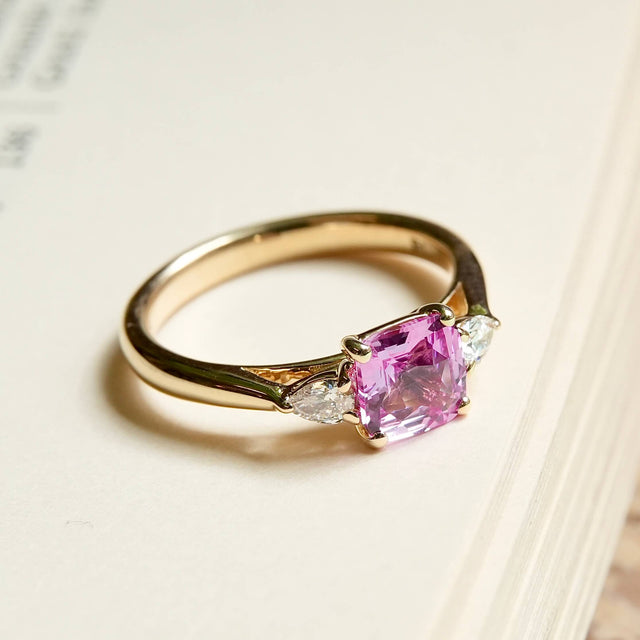 Emerald cut pink sapphire engagement ring with diamond side stones in yellow gold