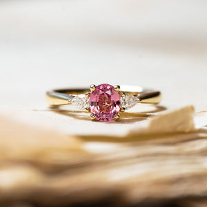 Pink sapphire and diamond three-stone engagement ring with oval pink sapphire and pear-shaped side diamonds.
