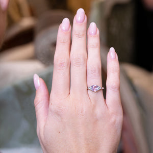 Pink sapphire and diamond cluster tre-foil engagement ring worn on hand.