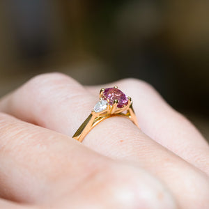 Pink sapphire and diamond three-stone engagement ring with polished gold band and diamond accents.