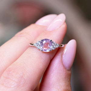 Pink sapphire and diamond cluster tre-foil engagement ring with diamond side clusters held between fingers.