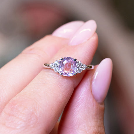 Pink sapphire and diamond cluster tre-foil engagement ring with diamond side clusters held between fingers.
