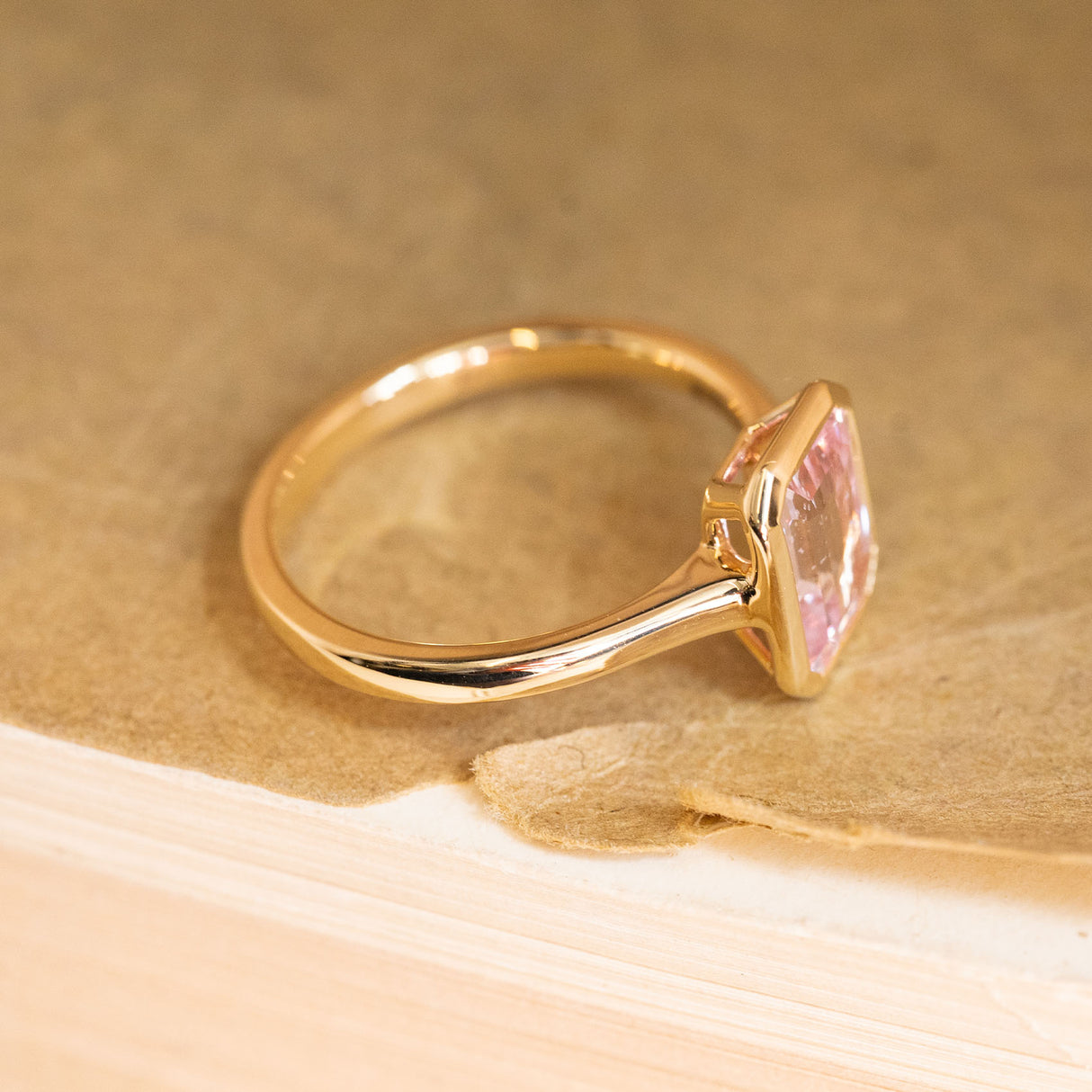 Solitaire engagement ring featuring a soft pink emerald-cut sapphire in a refined yellow gold design with contemporary styling.