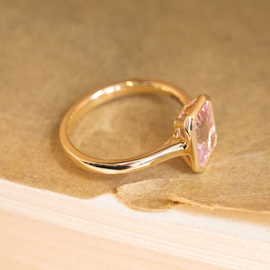 Solitaire engagement ring featuring a soft pink emerald-cut sapphire in a refined yellow gold design with contemporary styling.