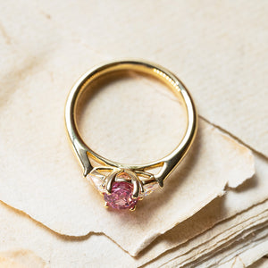 Pink sapphire and diamond three-stone engagement ring with polished gold band and open gallery detail.
