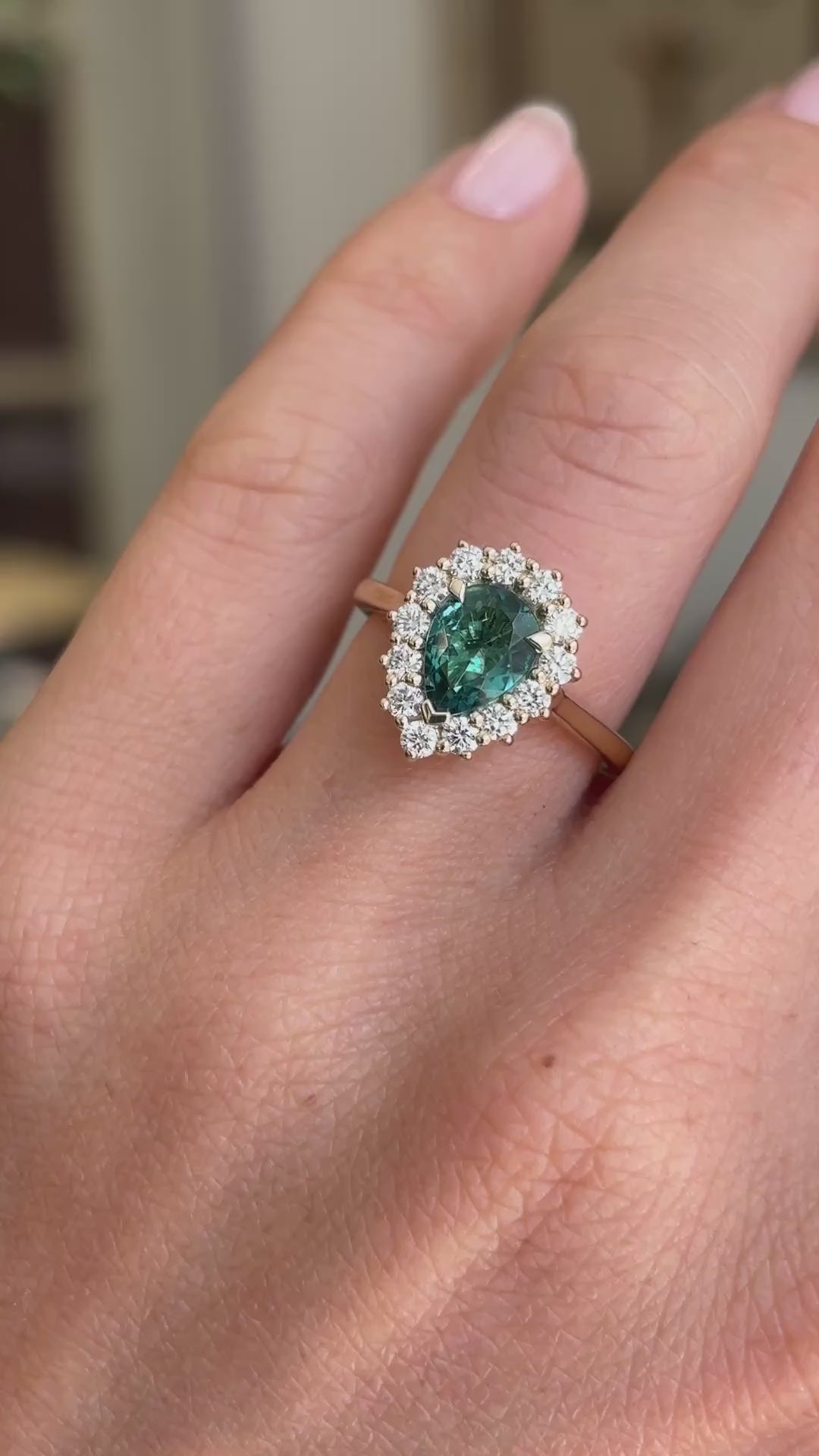 Antique-inspired pear-cut teal tourmaline and diamond cluster engagement ring featuring a pear-shaped teal tourmaline surrounded by brilliant-cut diamonds, displayed on a hand.