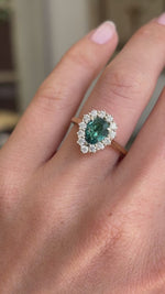 Antique-inspired pear-cut teal tourmaline and diamond cluster engagement ring featuring a pear-shaped teal tourmaline surrounded by brilliant-cut diamonds, displayed on a hand.