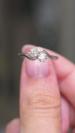 A video of an Antique, Edwardian toi et moi diamond two stone engagement ring crafted in platinum, held between fingers and rotated and turned to show various angles of the ring.