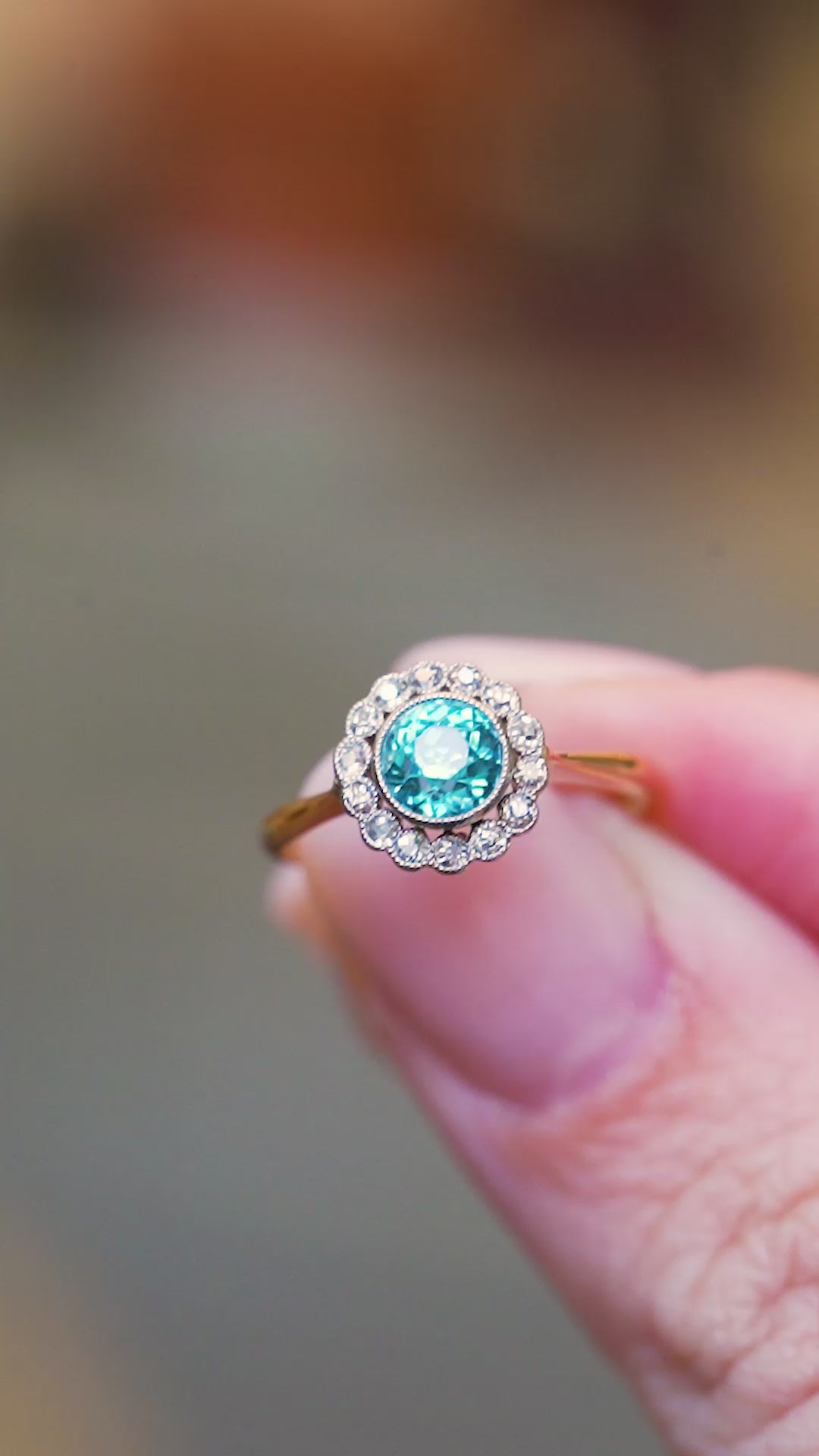 Antique cluster ring worn on hand with blue zircon and diamond surround.