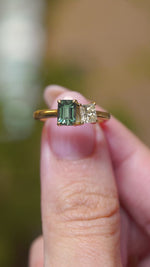 A video of a toi et moi green sapphire and diamond engagement ring held between fingers.