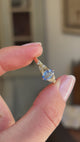 Blue sapphire and diamond engagement ring featuring an oval blue sapphire centre stone with diamond-set trefoil shoulders in the form of laurel leaves, held by hand for detailed viewing.