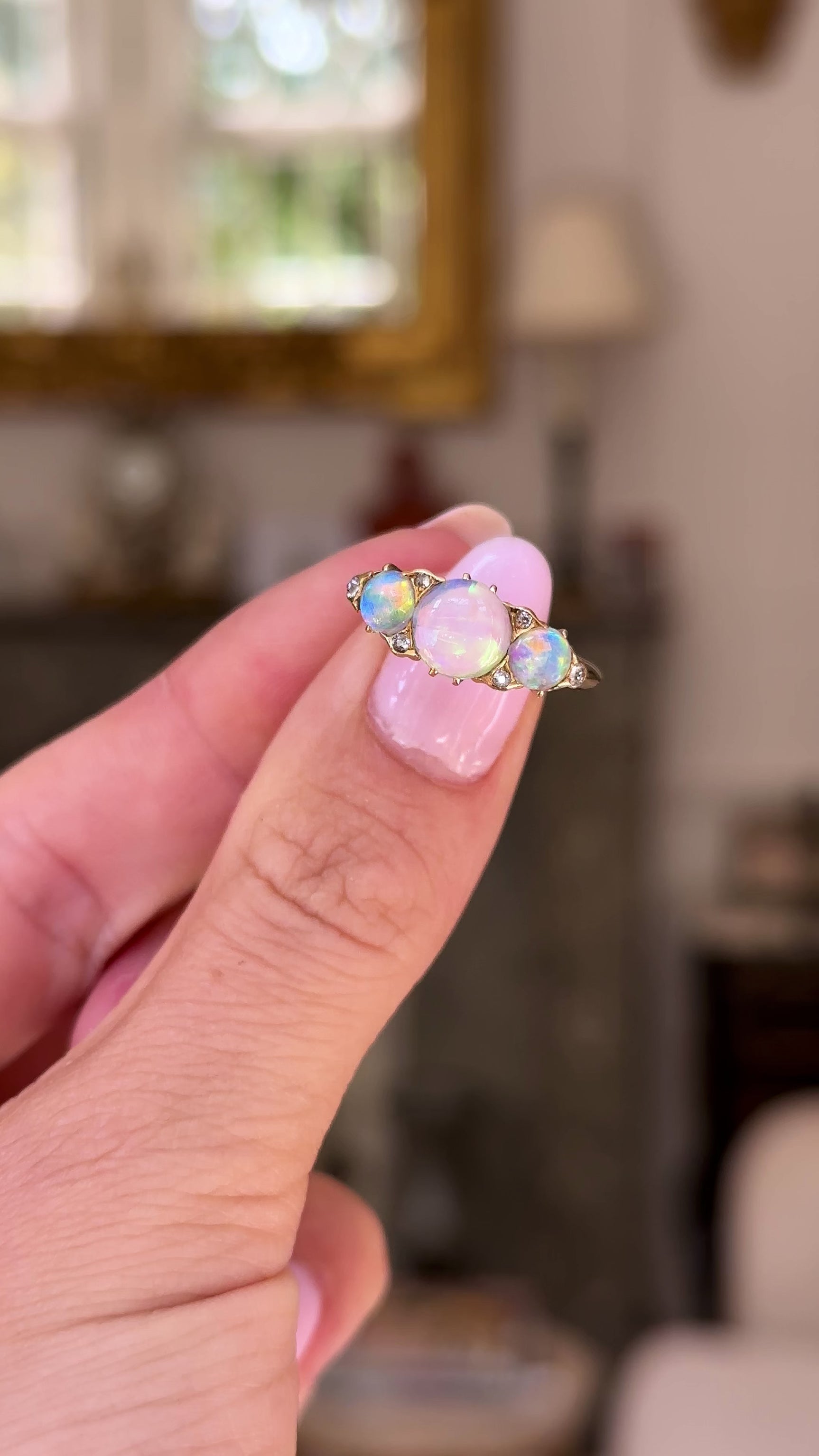 Opal and diamond three stone ring, held in fingers and rotated to give perspective, front view. 