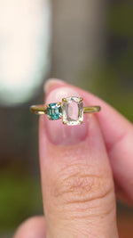 A video of an Antique-inspired, colourless and teal-blue Sapphire toi et moi two stone engagement ring on a yellow gold band, held between the fingers and turned to showcase different angles.