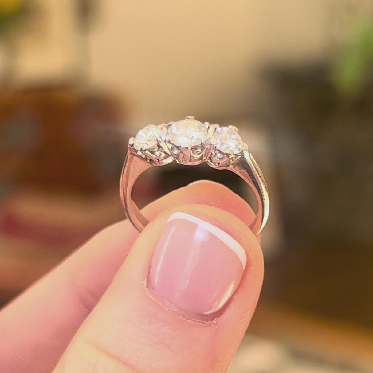Vintage diamond three stone ring in white gold held in between the fingers and turned to show different angles of the ring,