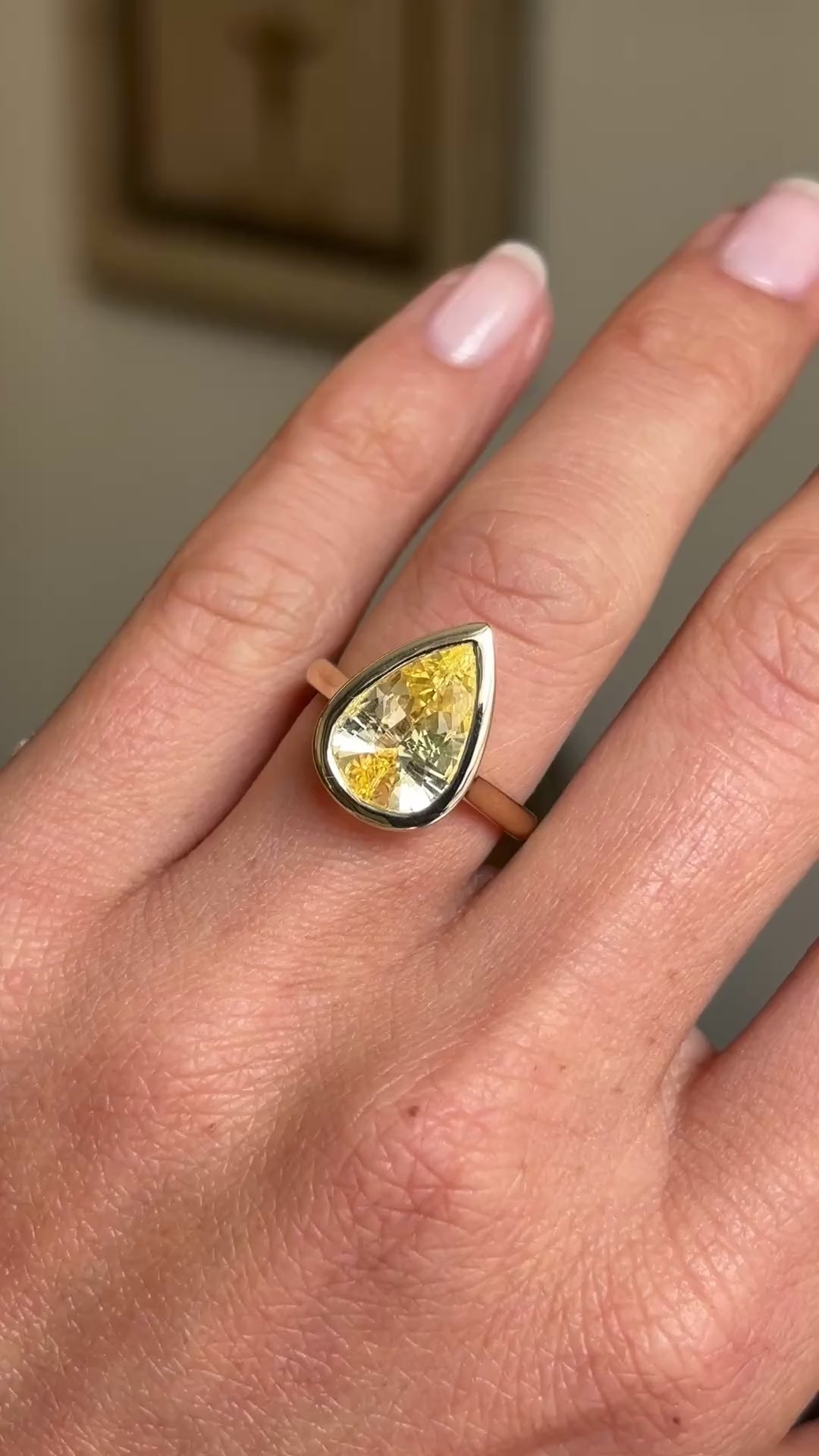 Antique-inspired yellow gold solitaire ring worn on hand, featuring a large pear-cut Sri Lankan yellow sapphire in a smooth rub-over setting, showcasing its rich golden colour against a softly lit vintage interior backdrop.