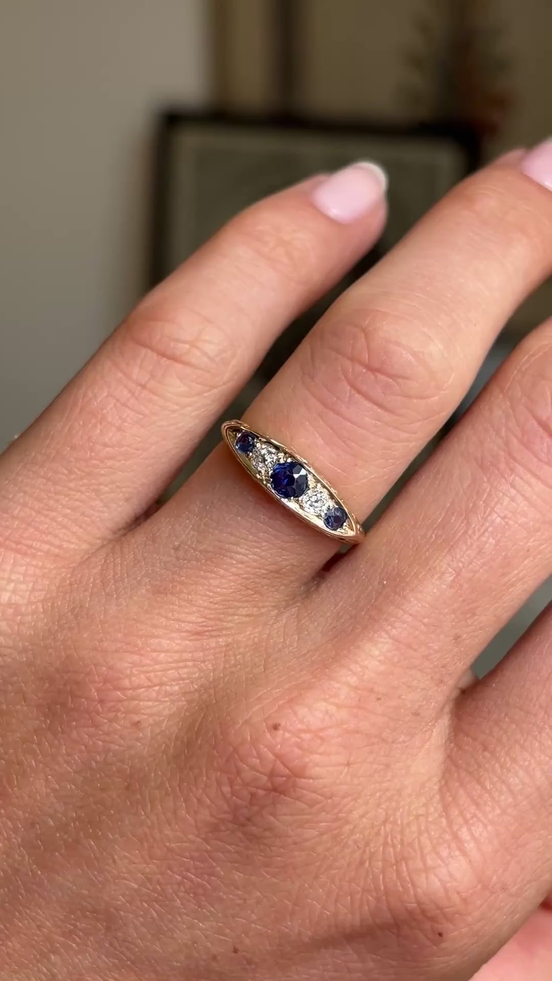Video of an Antique, Victorian sapphire & diamond five-stone engagement ring in yellow gold worn on a hand against a blurred background.