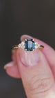 A close-up of a yellow gold ring with a teal sapphire and diamond cluster.