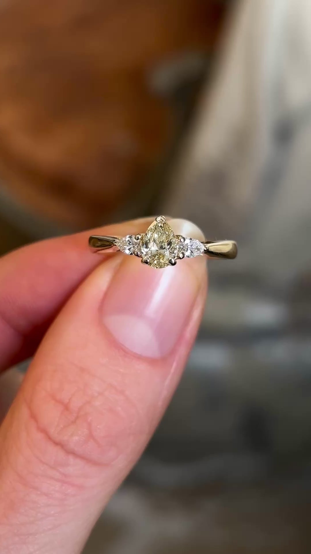 Pear-cut diamond three-stone engagement ring held in fingers and rotated showing diamond colours and clarity. 