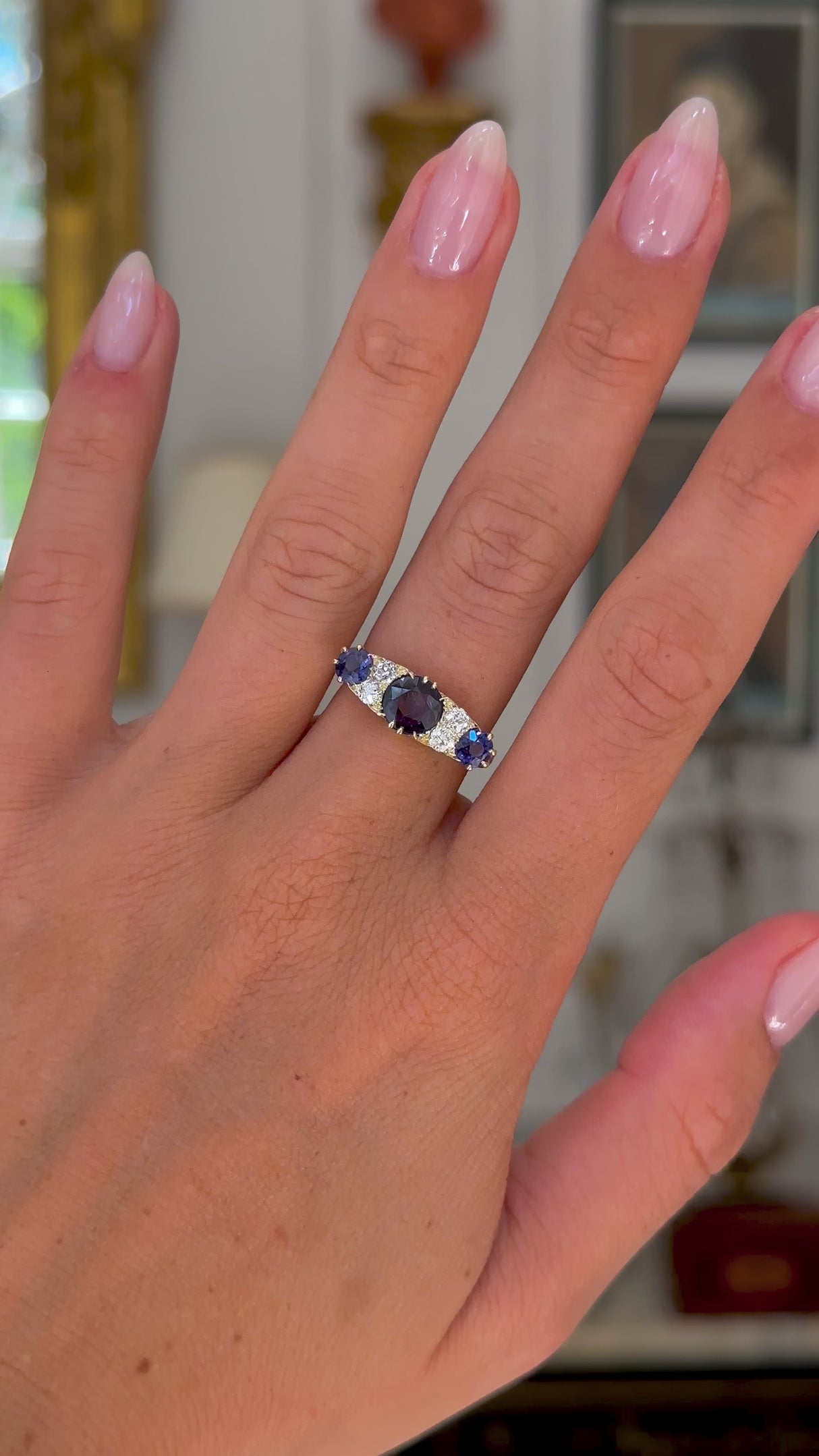 Antique purple sapphire and diamond engagement ring, worn on hand and moved away from lens to give perspective, front view.