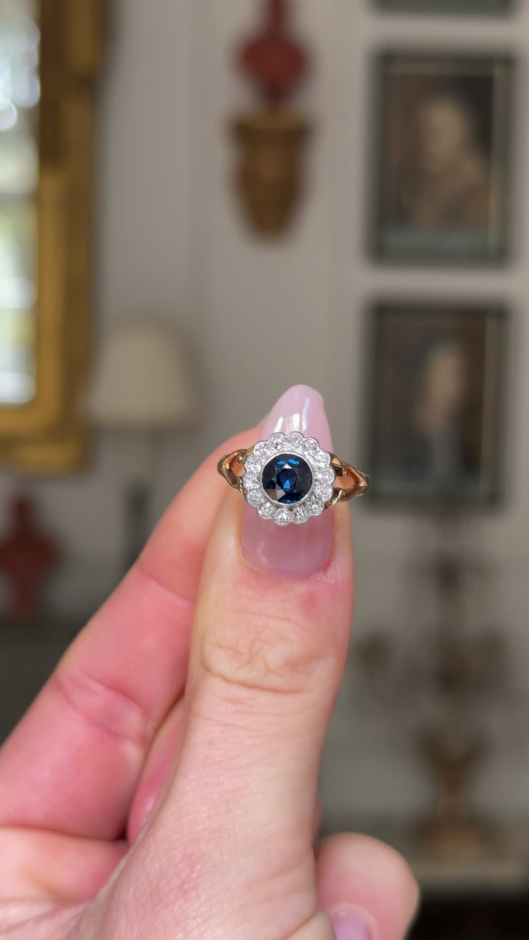 Antique sapphire diamond cluster ring, held in fingers and rotated to give perspective, front view. 