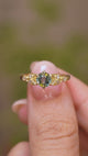 A close up video of a Vintage-inspired, Green sapphire and diamond engagement ring in yellow gold held between two fingers and rotated slowly to display all the profiles of the ring.