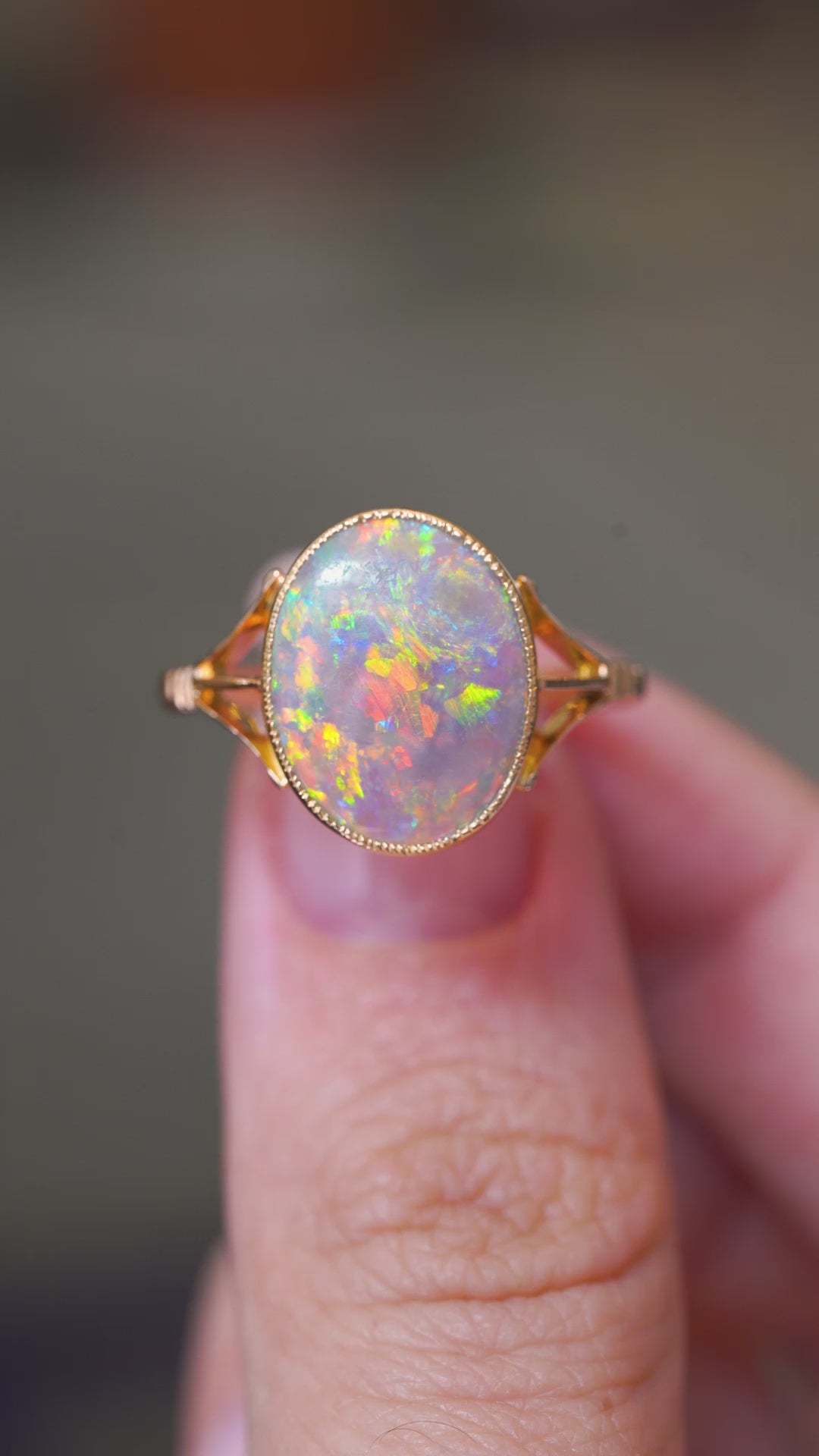 A video of an antique, Edwardian era oval opal single stone ring with decorative split shoulders mounted in yellow gold and held between the fingers as it is turned to show the different angles and details of the ring.