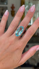aquamarine and yellow gold cocktail ring on left hand, middle finger. Shot with hand up close and moving away from lens, and antiquated bokeh background. 