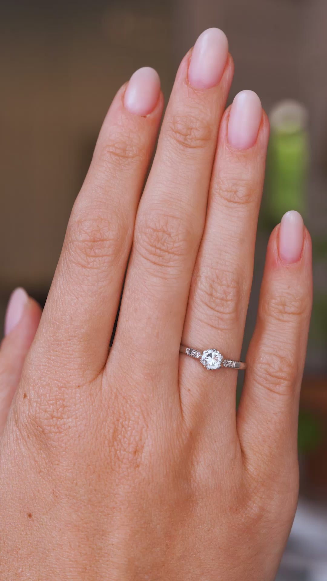 Close up video of a hand wearing an Antique, 1930s Art-Deco diamond flanked solitaire engagement ring in platinum.  Worn on a wedding finger and rotated slowly to show the profiles once worn. 