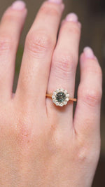 A video of an earthy green sapphire and diamond engagement ring displayed on the hand in an antique-inspired yellow gold setting.