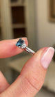 Video of a Vintage-inspired, Teal sapphire and diamond three-stone engagement ring in platinum held by two fingers and rotated to show the profile