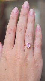 A video of a hand wearing an antique-inspired, light Pink sapphire solitaire engagement ring, the hand is stretched out and slowly turned against a blurred background.
