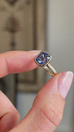 A close-up video of an antique-inspired, purple-blue sapphire solitaire engagement ring held between fingers showing a side-to-side motion.