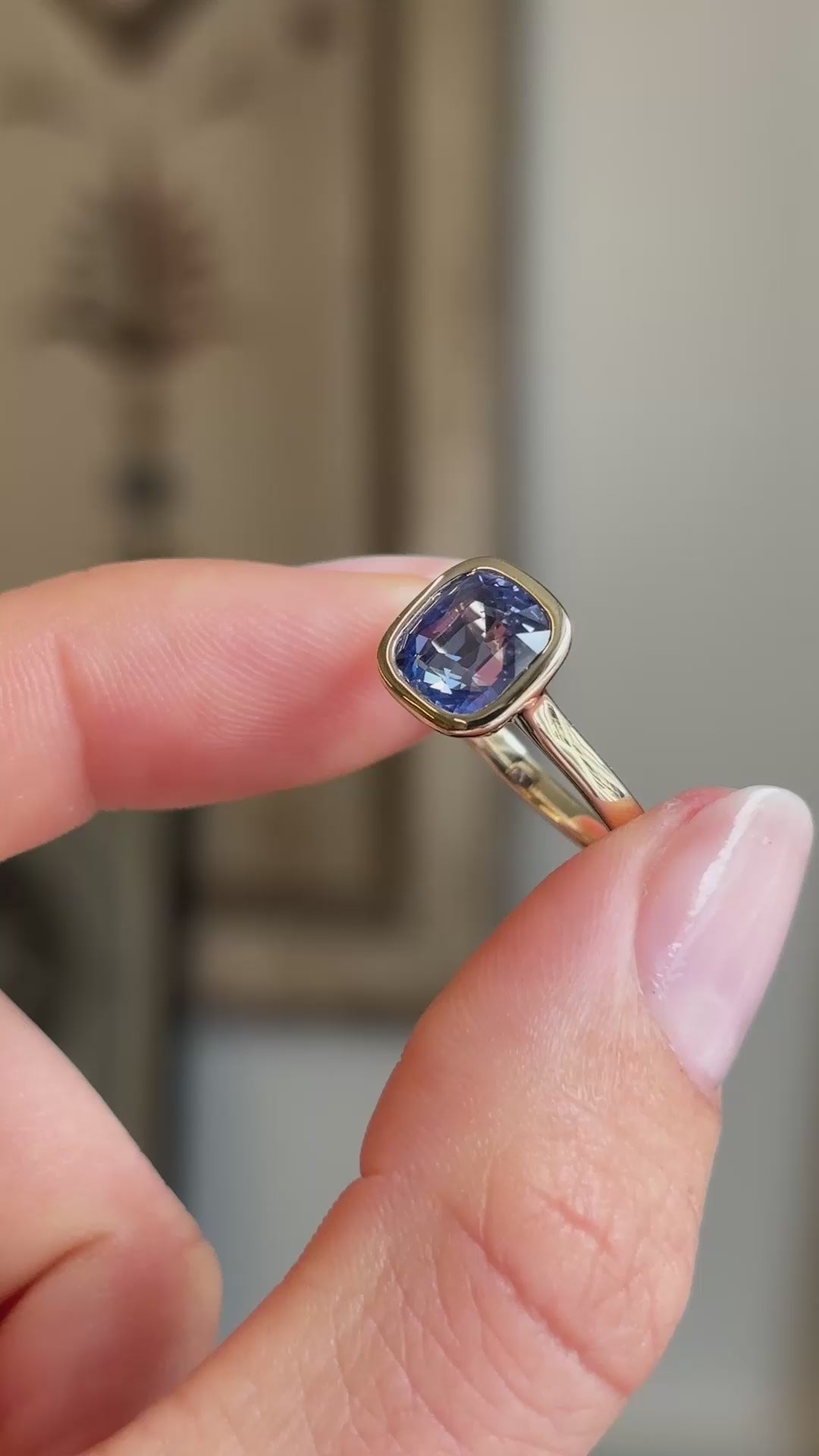A close-up video of an antique-inspired, purple-blue sapphire solitaire engagement ring held between fingers showing a side-to-side motion.