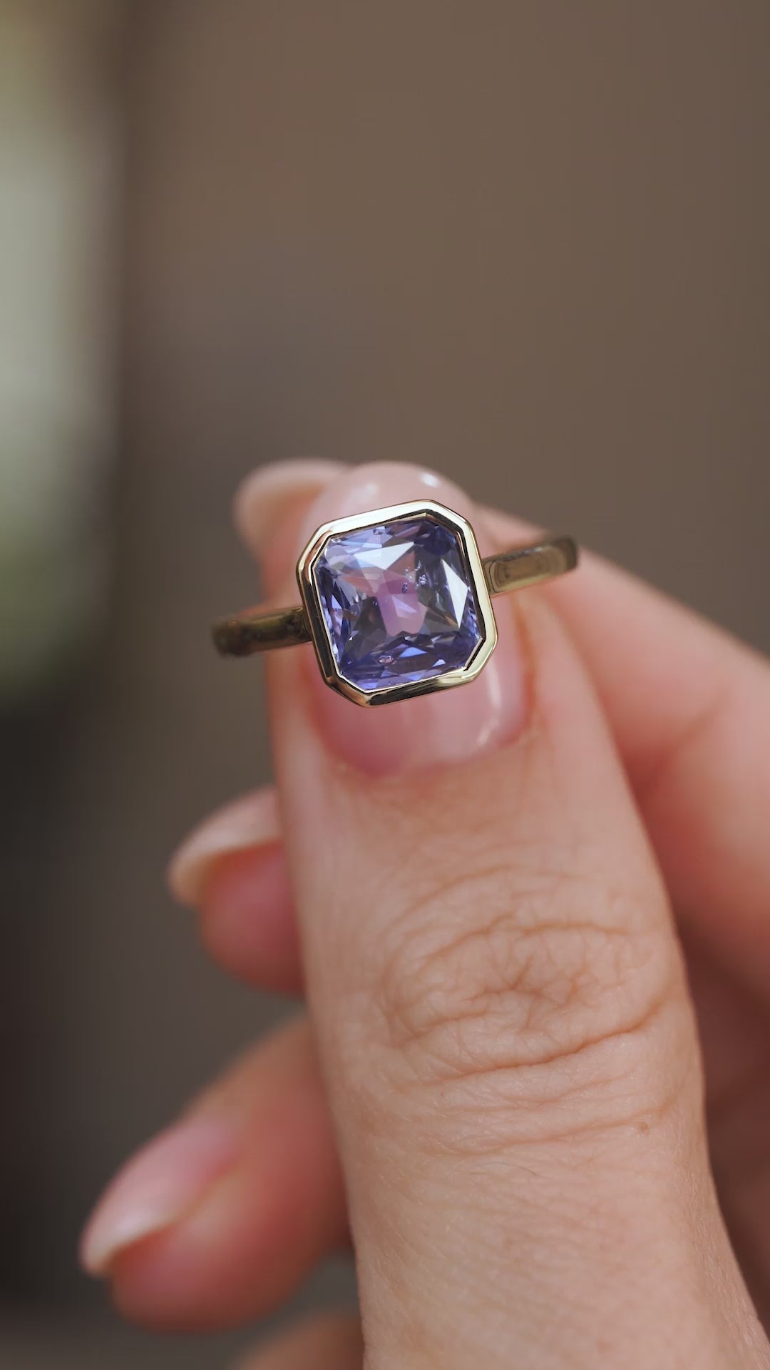 Video close-up of the blue-purple sapphire ring balanced on a fingertip, highlighting its colour and clean lines.