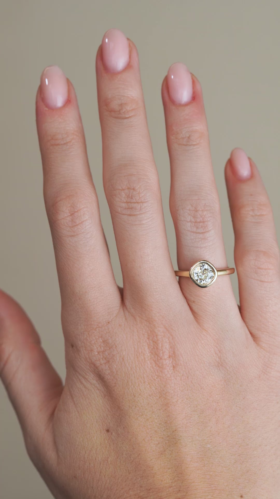 A video of the old mine-cut diamond engagement ring worn on a finger, capturing the stone's broad facets and warm reflections within its gold setting.