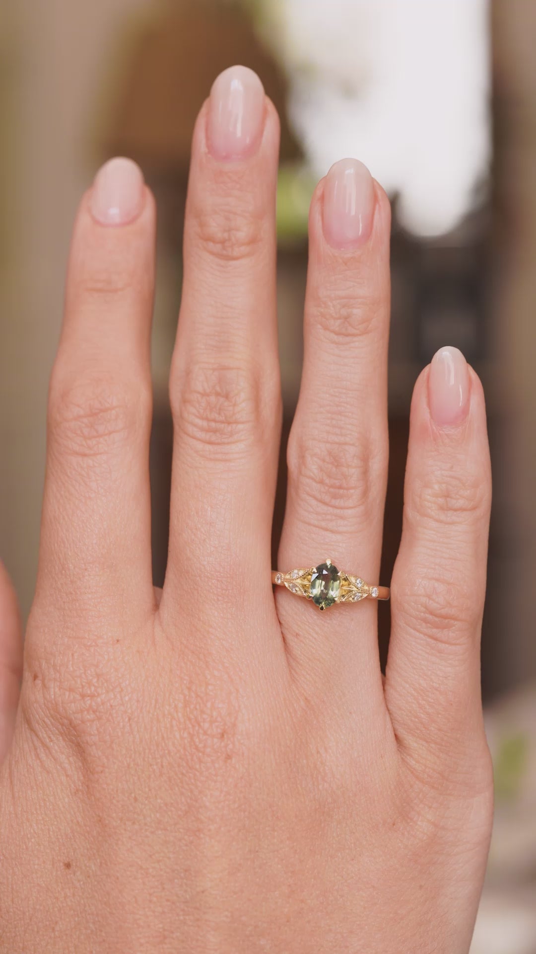 A video of a Vintage-inspired, Green sapphire and diamond engagement ring worn on the hand from a distance.