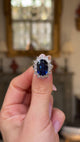 A vintage sapphire and diamond cluster ring held in fingers and moved around to give perspective.