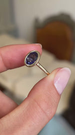 An antique-inspired, royal purple oval sapphire solitaire ring in 14ct yellow gold shown in video, held between fingers.