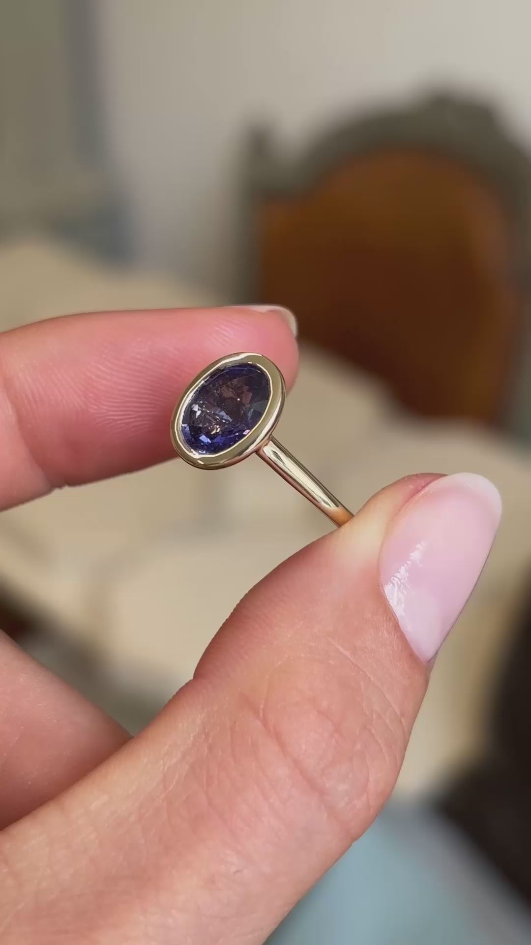 An antique-inspired, royal purple oval sapphire solitaire ring in 14ct yellow gold shown in video, held between fingers.