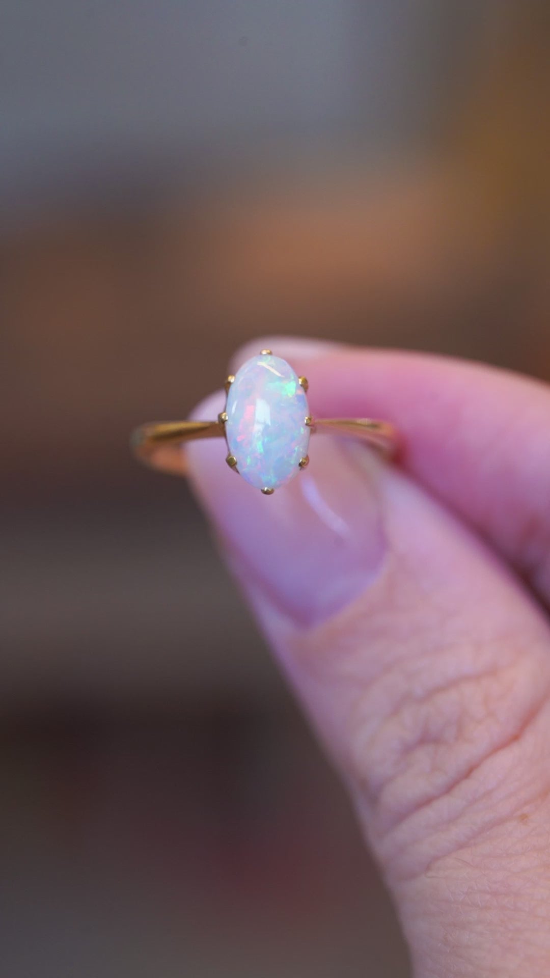 Close detail video of precious opal solitaire ring with iridescent oval opal and gold setting.