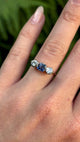 Antique, Edwardian sapphire and diamond three-stone engagement ring worn on hand.