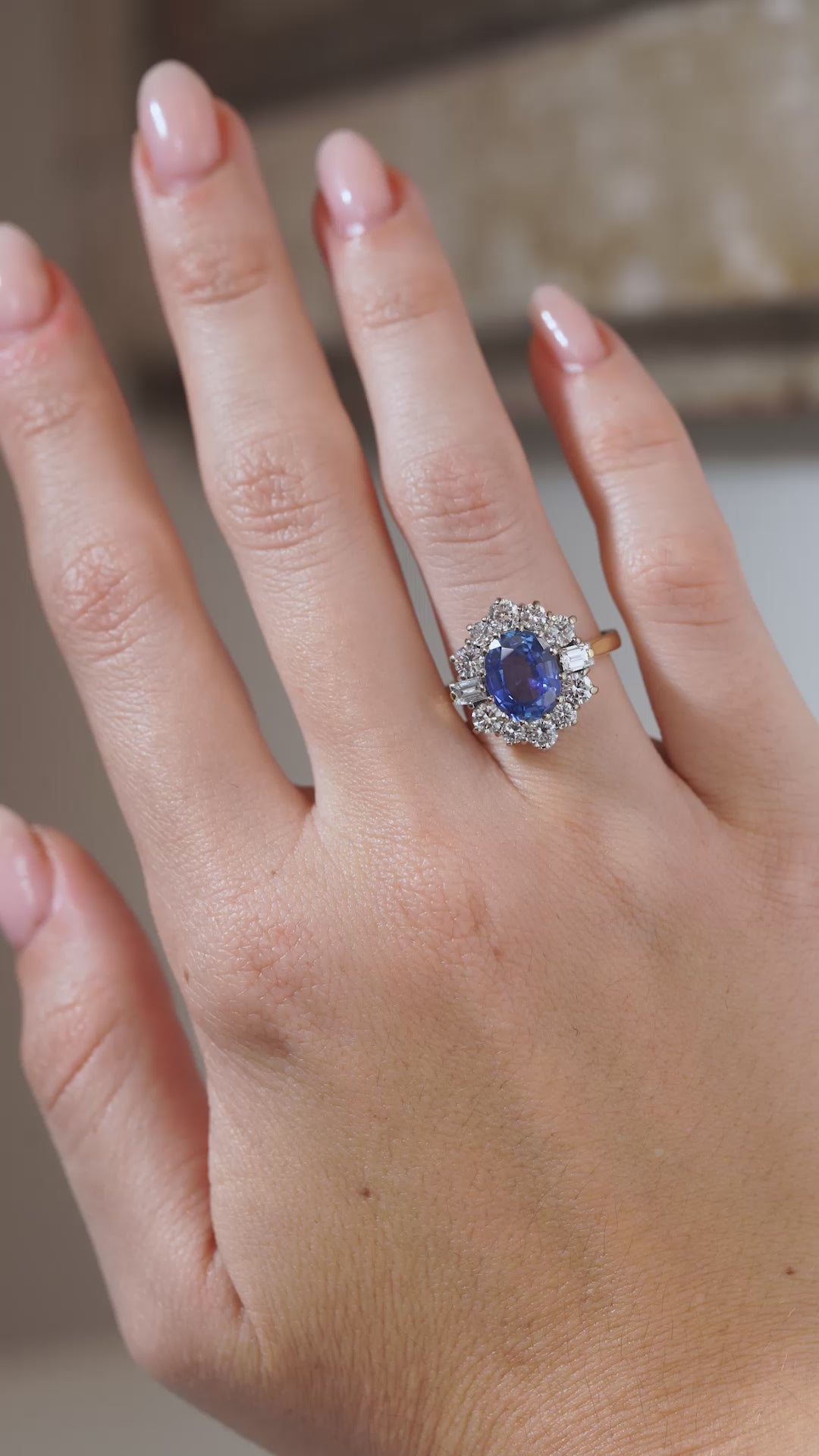 A close-up video of a vintage 1980s blue sapphire and diamond cluster ring modelled on a hand, highlighting the oval sapphire, diamond-set platinum cluster and yellow gold band.