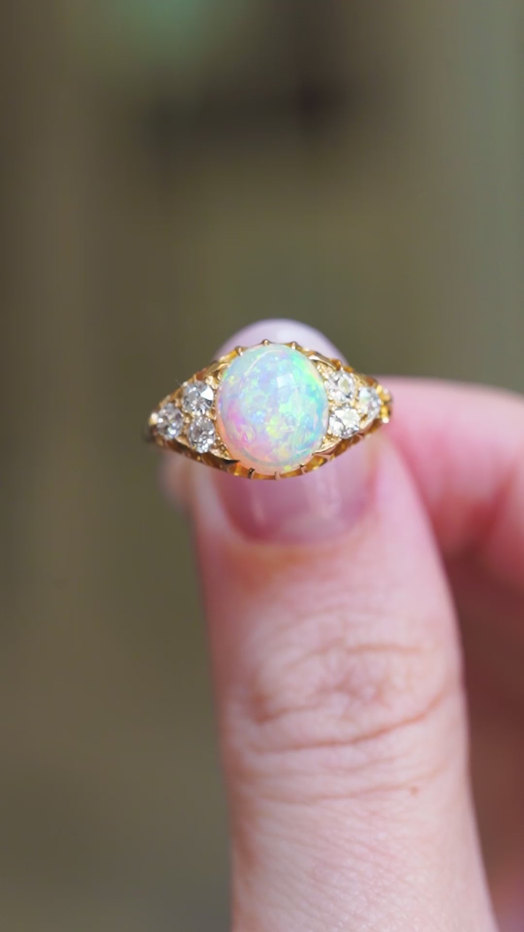 Antique Victorian opal and diamond ring showing iridescent opal and diamond cluster detail between fingers.