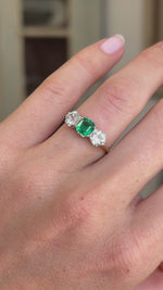 Antique Edwardian emerald and diamond three-stone engagement ring featuring an emerald centre stone flanked by two diamonds, displayed on a hand.