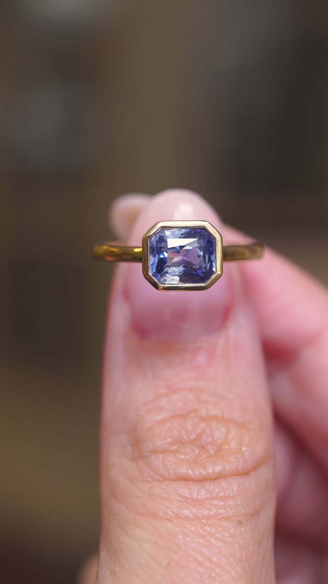 A video of a close detail of an antique-inspired blue sapphire solitaire ring crafted in yellow gold held between fingers.