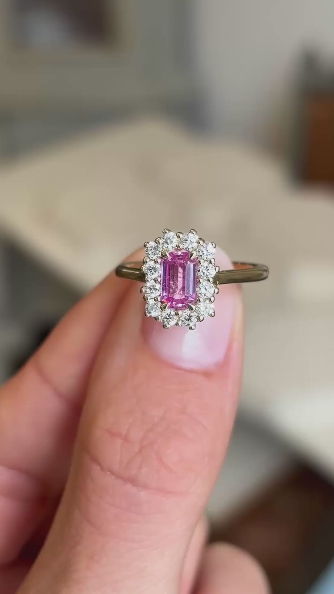 A close-up video of an antique-inspired, pink sapphire and diamond halo cluster set in 14ct yellow gold held between fingers.