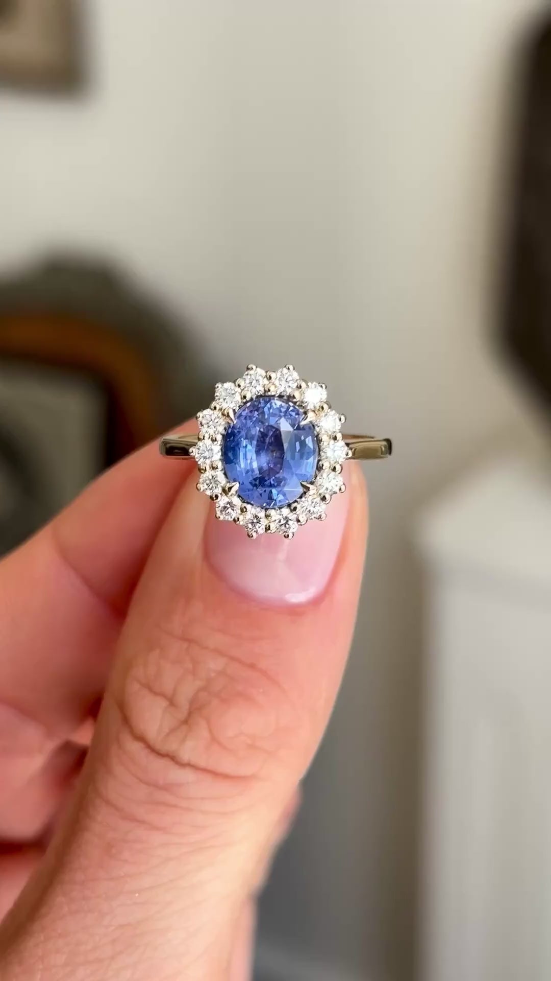 Antique-inspired intense cornflower blue sapphire and diamond cluster engagement ring showcasing an oval cornflower blue sapphire, diamond halo and elegant gallery setting, held by hand.