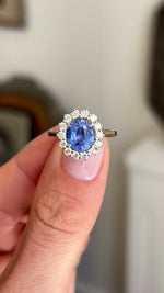 Antique-inspired intense cornflower blue sapphire and diamond cluster engagement ring showcasing an oval cornflower blue sapphire, diamond halo and elegant gallery setting, held by hand.